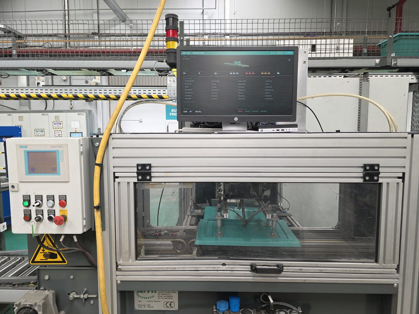 AMI lidding machine on a factory floor with the original Siemens TP177A touch panel on the left and a new custom production dashboard on an HP monitor mounted above the machine, with the HP EliteDesk industrial PC visible below