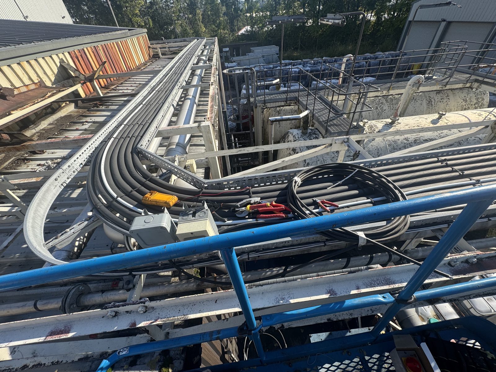 Heat trace cables being routed along an elevated pipe rack at the Norit facility, with tools, cable coils, and junction boxes visible on the cable tray