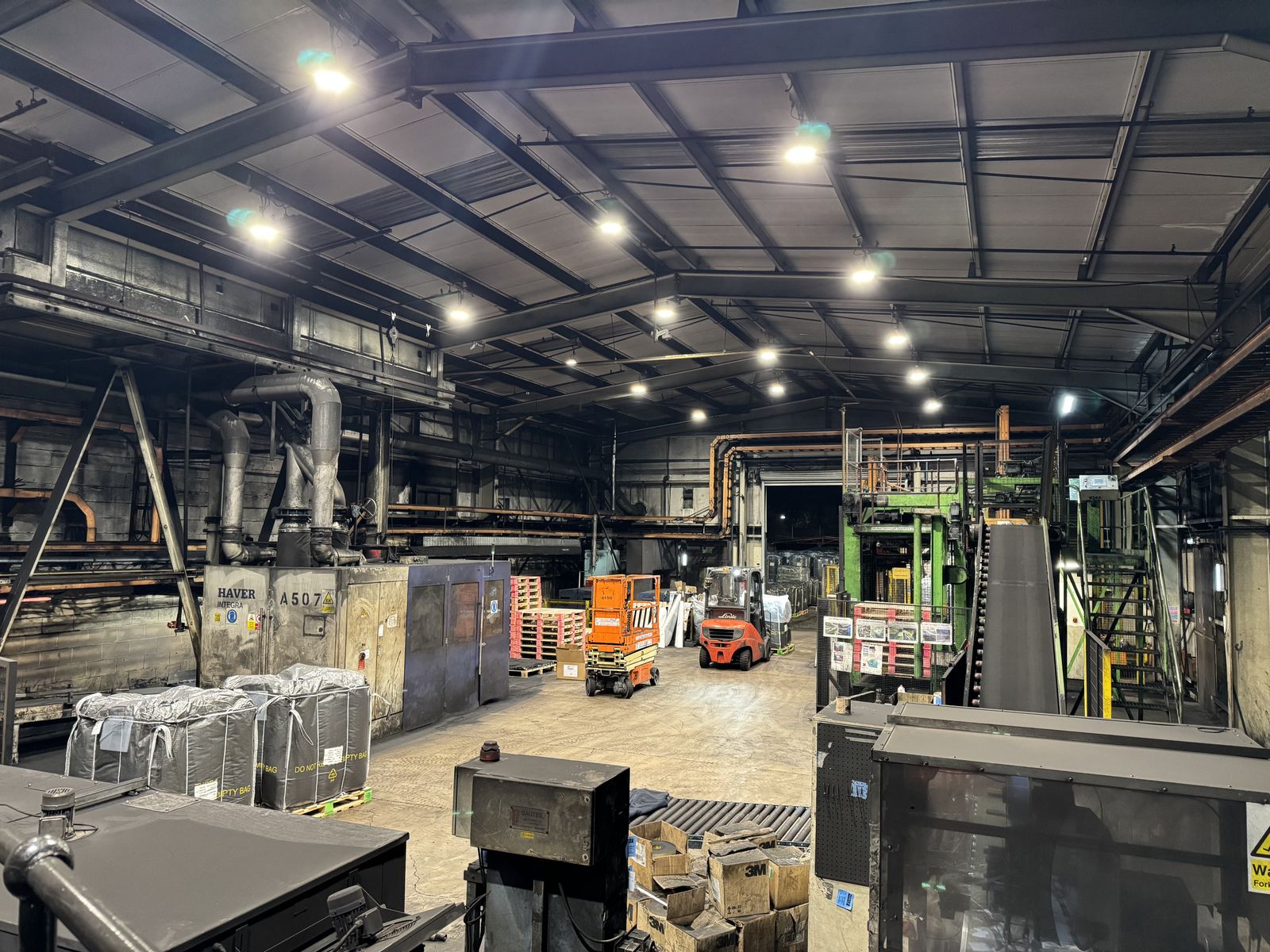 Norit Activated Carbon warehouse interior after LED retrofit showing bright white light from new 200W LED high bays illuminating production equipment, forklift, and scissor lift